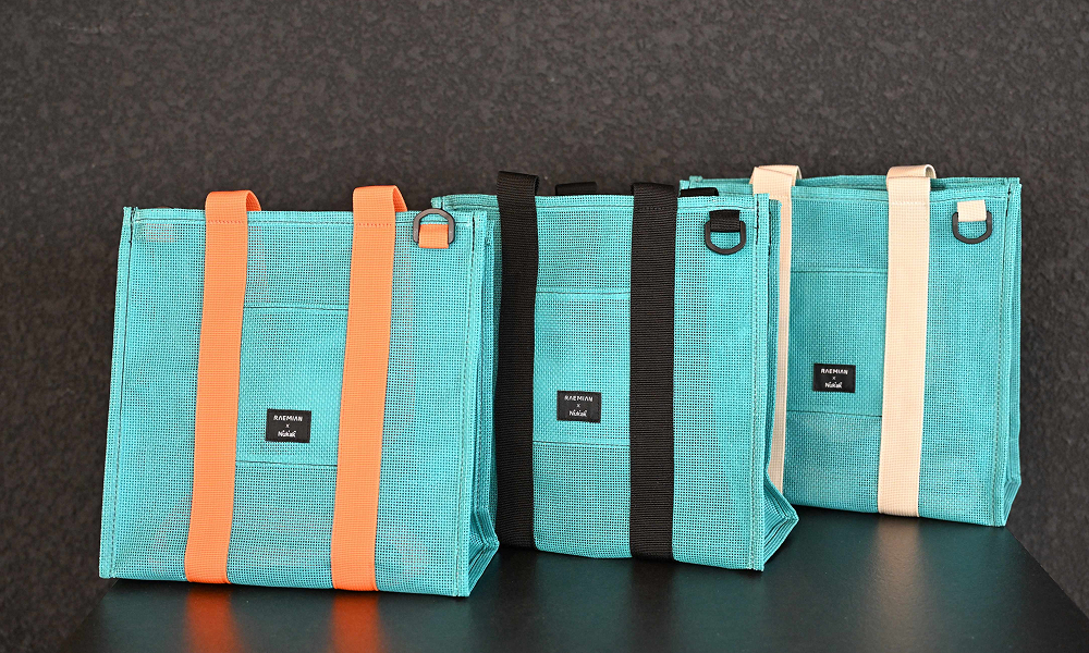 A set of upcycled tote bags made from repurposed construction waste materials. The bags are turquoise with orange and black straps, part of Samsung C&T E&C Group’s Raemian upcycling collection, designed to promote sustainability and reduce waste.