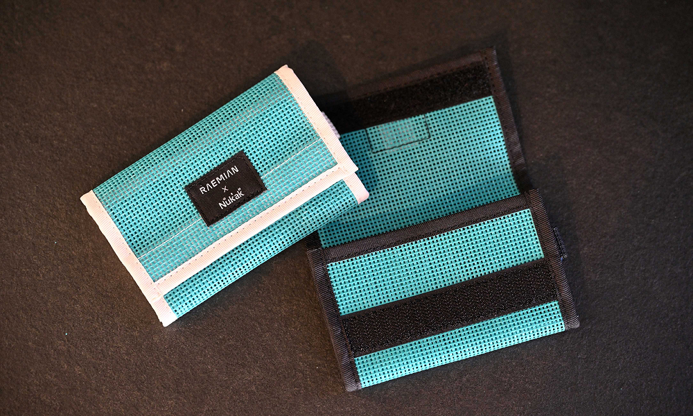 Two upcycled card wallets from Samsung C&T E&C Group’s Raemian upcycling collection, made from turquoise construction safety netting. The wallets feature black and white fabric accents, showcasing the creative reuse of materials from construction sites.