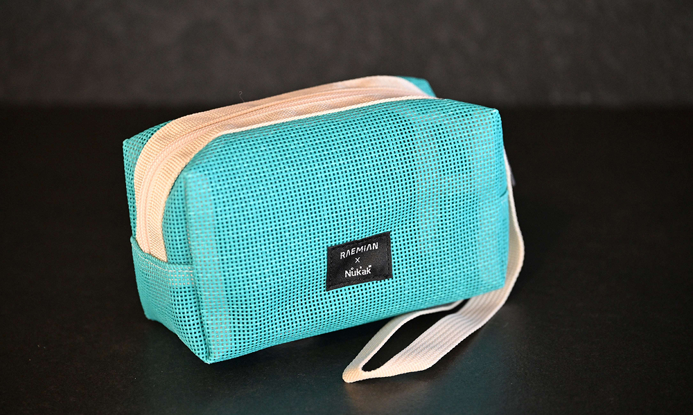 A compact upcycled pouch made from turquoise construction safety netting, part of Samsung C&T E&C Group’s award-winning Raemian upcycling collection. The pouch has a white zipper and beige fabric accents, demonstrating a stylish and functional design.