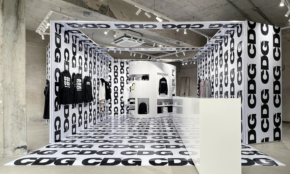 A pop-up store featuring the CDGCDGCDG line by COMME des GARÇONS, with bold "CDG" branding covering the walls, floor, and ceiling. The space reflects the line’s streetwear influence with minimalist clothing displays