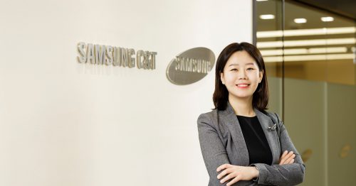 Jungwan Kim poses with arms crossed, smiling beside a wall with the Samsung C&T logo at company headquarters.