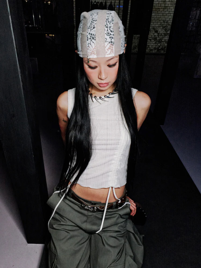 Jisoo Seo wears a white shirred tank top with drawstrings and a beanie, styled with loose low-rise cargo pants and layered chain accessories.