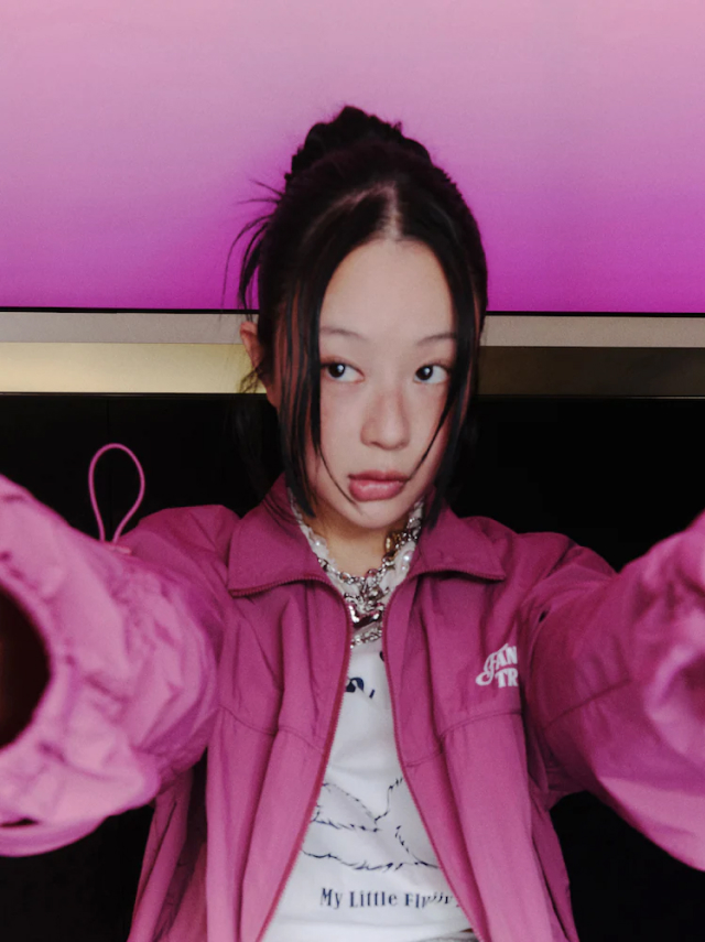 Jisoo Seo takes a selfie in a magenta windbreaker and chunky chain necklace, with a cropped graphic tee.