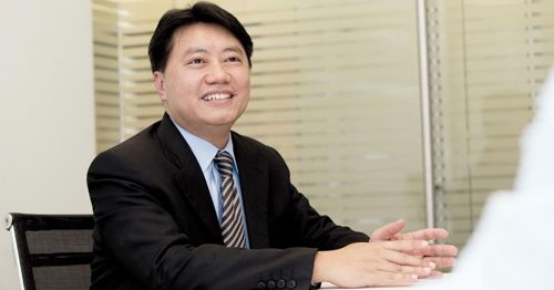 Chaimongkol Worapinpong seated in a meeting room, smiling while speaking during an interview.