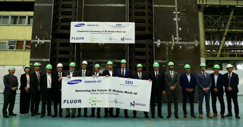 A group of representatives from the Romanian SMR Project pose for a photo in front of a large SC module at IHI's Yokohama plant. They hold banners reading "Completion Ceremony of SC Module Mockup" and "Delivering the Future: SC Module Mockup" for the RoPower SMR Romania Project.