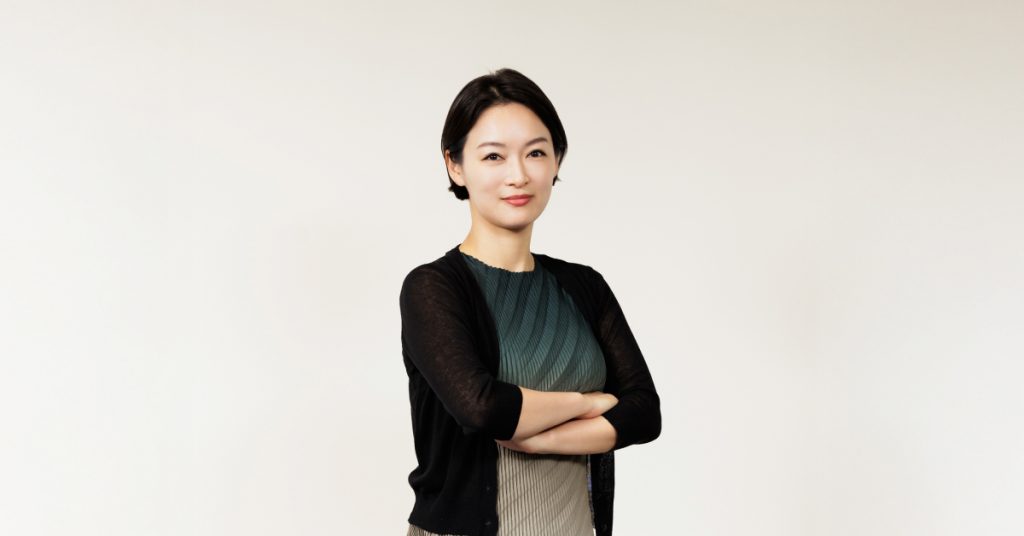 Samsung C&T Trader Soh-young Cecilia Lim poses confidently against a plain white background, arms crossed, wearing a pleated green dress with a black cardigan.