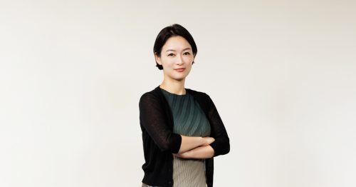 Samsung C&T Trader Soh-young Cecilia Lim poses confidently against a plain white background, arms crossed, wearing a pleated green dress with a black cardigan.
