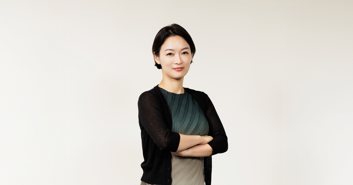 Samsung C&T Trader Soh-young Cecilia Lim poses confidently against a plain white background, arms crossed, wearing a pleated green dress with a black cardigan.