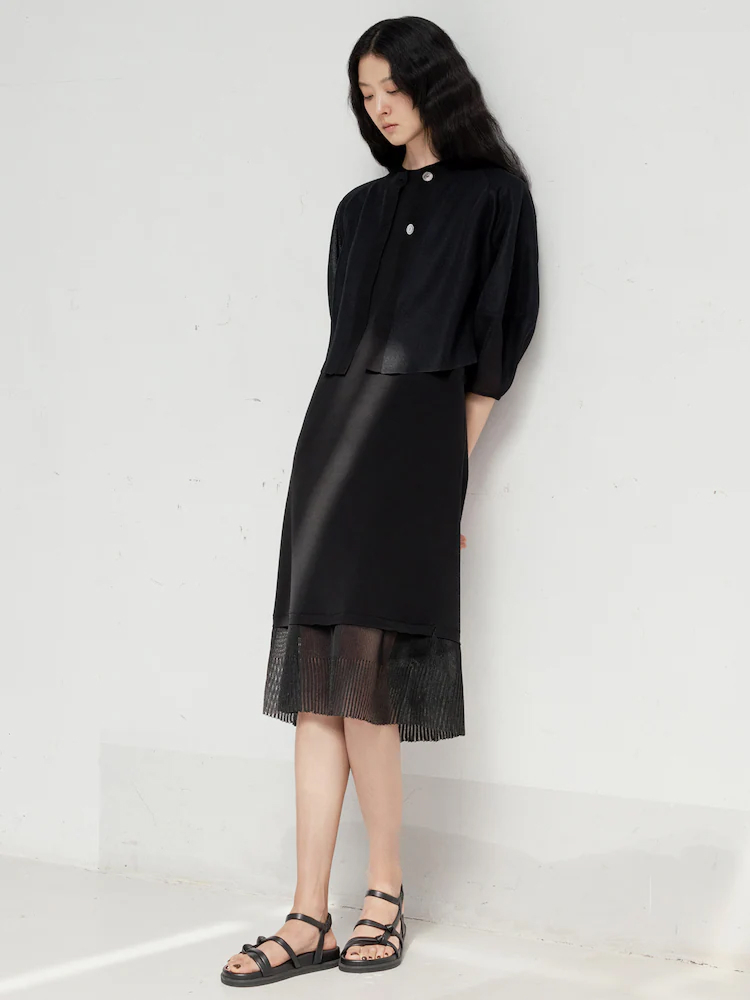 Model wears the LEBEIGE black knit dress featuring sheer pleated hem details, styled with black sandals in a minimalist space.