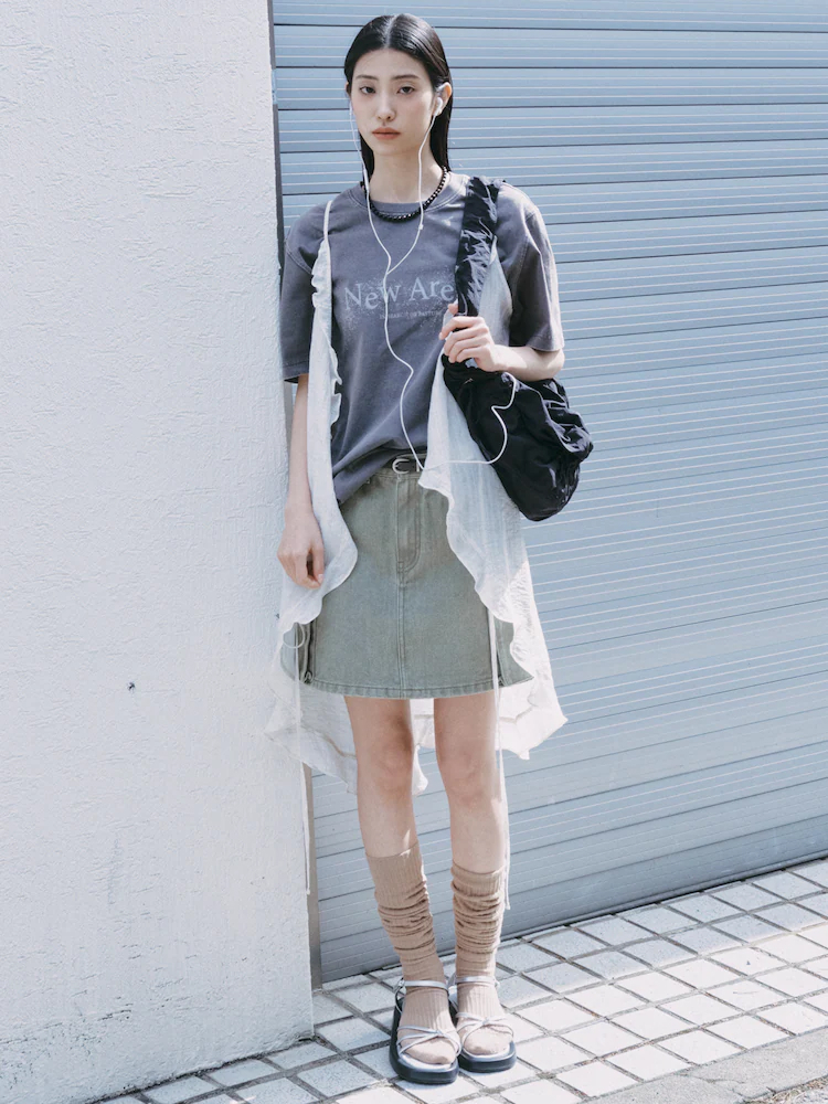 Model wears the khaki cargo skirt with a graphic tee and sheer vest, styled with layered socks and sandals.