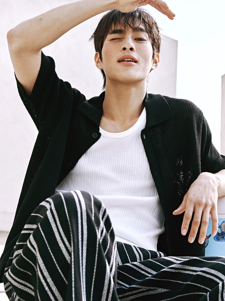 Male model wears the 8seconds black collar knit cardigan over a white tank and striped trousers, seated under bright sunlight.