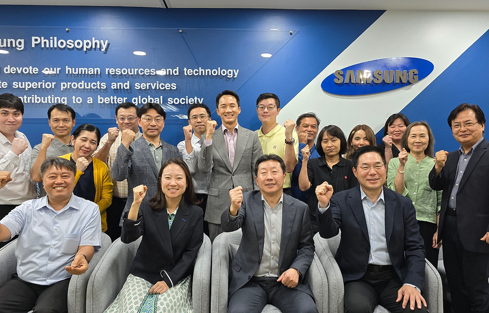 Group photo of Samsung C&T Bangkok office staff standing and seated in front of the company’s blue wall and slogan.