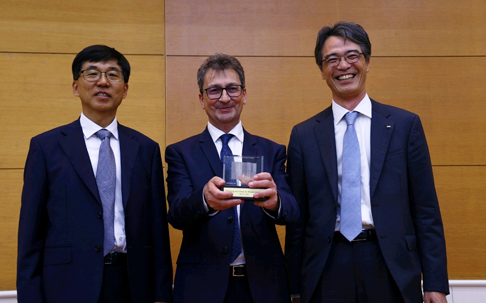 Three men in suits, including representatives from Samsung C&T, RoPower, and IHI, pose smiling indoors while the man in the middle holds a commemorative glass award.