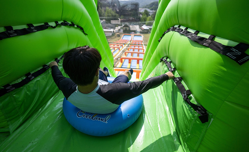 Person sitting in a blue Everland tube at the top of a tall green inflatable slide, preparing to go down.