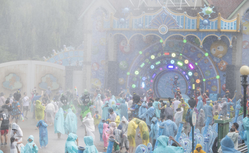 Visitors in ponchos enjoying a splash show in front of a stage with bright lights and animated characters.