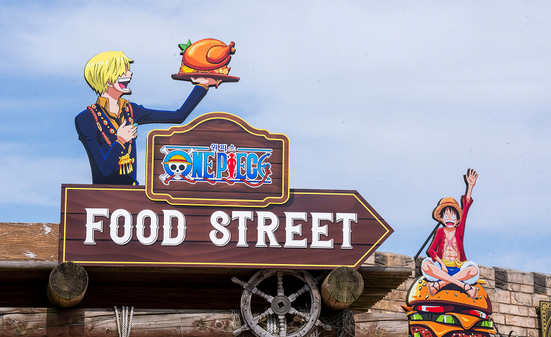 Decorative sign for “One Piece Food Street” featuring Sanji holding a roast chicken and Luffy sitting on a burger.