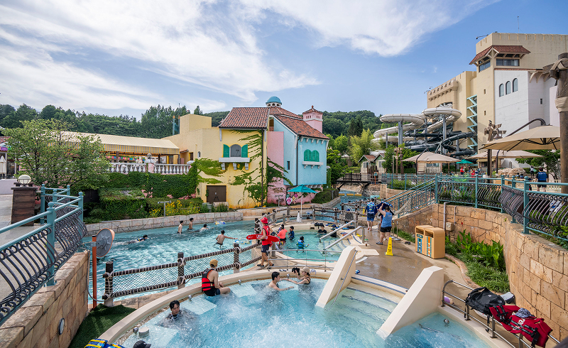 People relaxing in a pool surrounded by colorful buildings and water slides at Caribbean Bay.