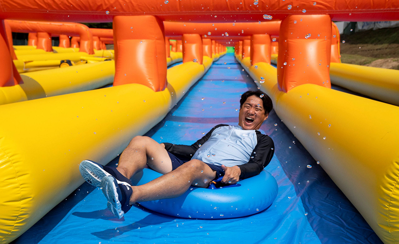 Man laughing while riding an inflatable tube down a colorful water slide with splashes around him.