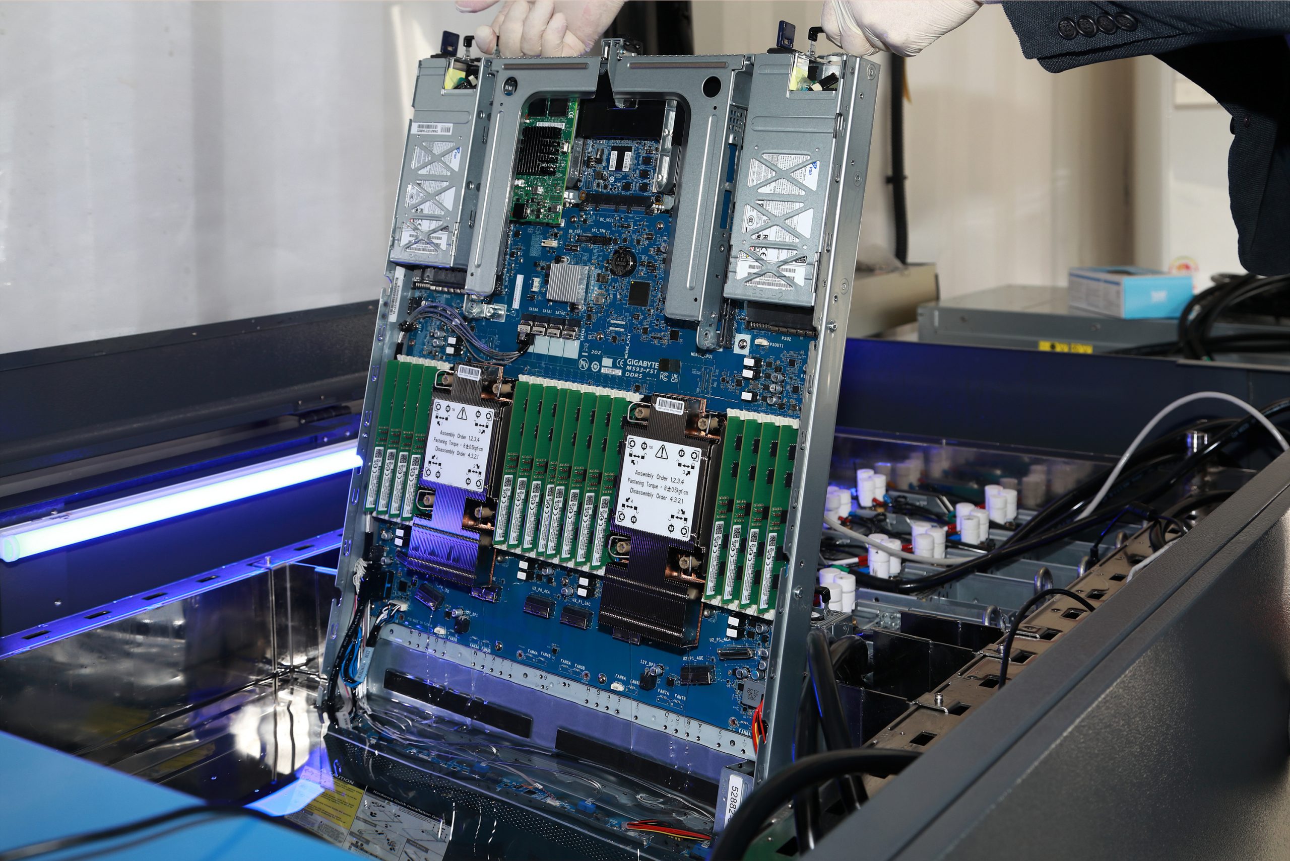 Gloved hands lowering a server into an immersion cooling tank containing dielectric coolant.