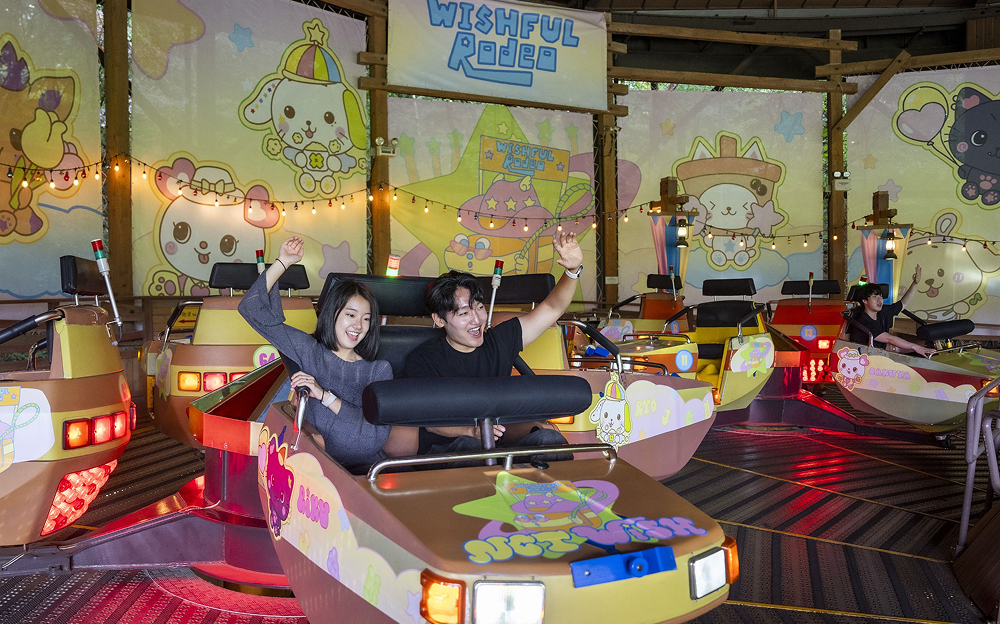 Visitors enjoying the NCT WISH-themed "Wishful Rodeo" ride at Everland, surrounded by cute, colorful character backdrops and vibrant lighting.