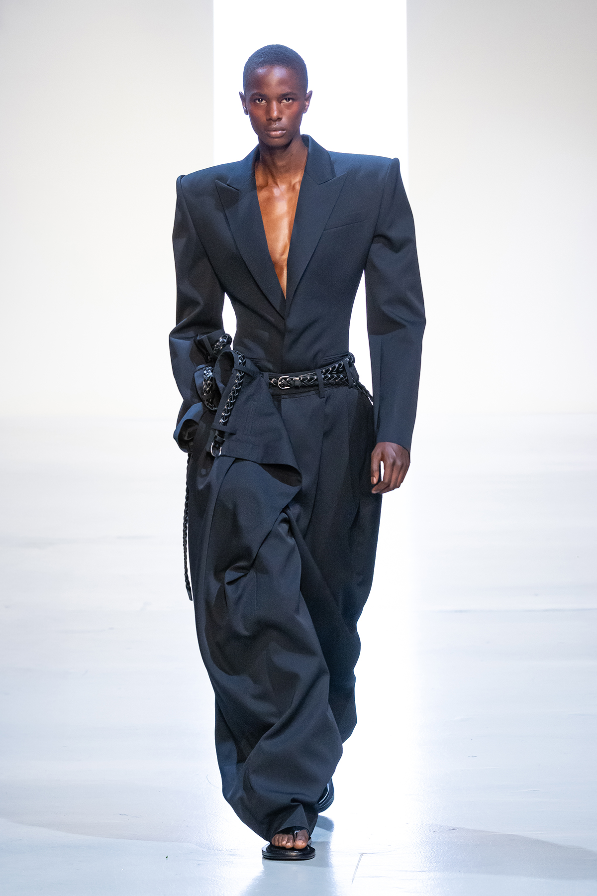 A model showcases Juun.J’s 26SS look featuring a sharp-shouldered tailored black blazer paired with voluminous wide-leg trousers and a belted waist, highlighting bold contrasts and modern structure.