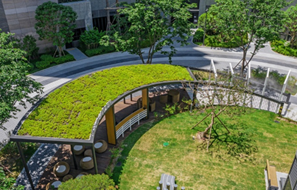 Wide view of the Mist Garden at Dongnae Raemian I-Park, featuring a green-roofed curved shelter, circular benches, and surrounding trees and plants.