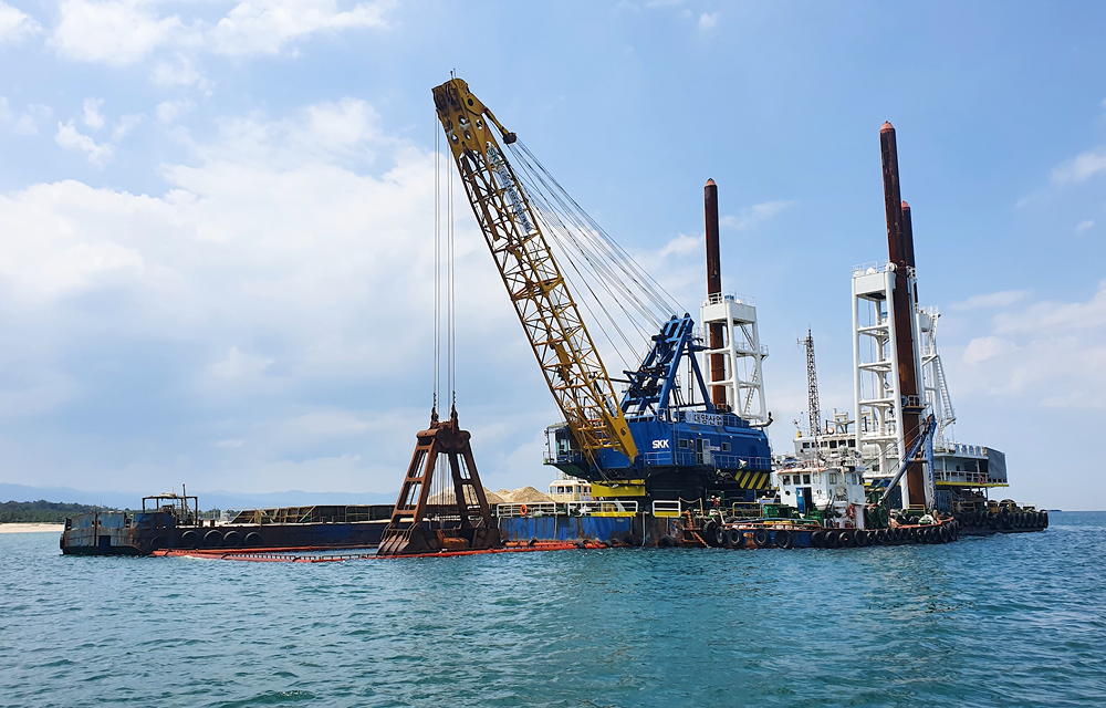 Offshore construction vessel equipped with a large crane operating at the Gangneung site. The project is near completion, with the coastline visible in the background.