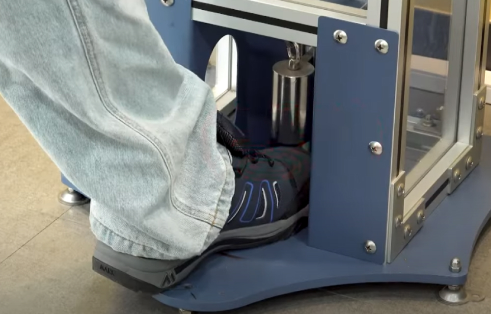 A man places his foot wearing safety boots into a device where a weight will be dropped to experience the protectiveness of the boots.
