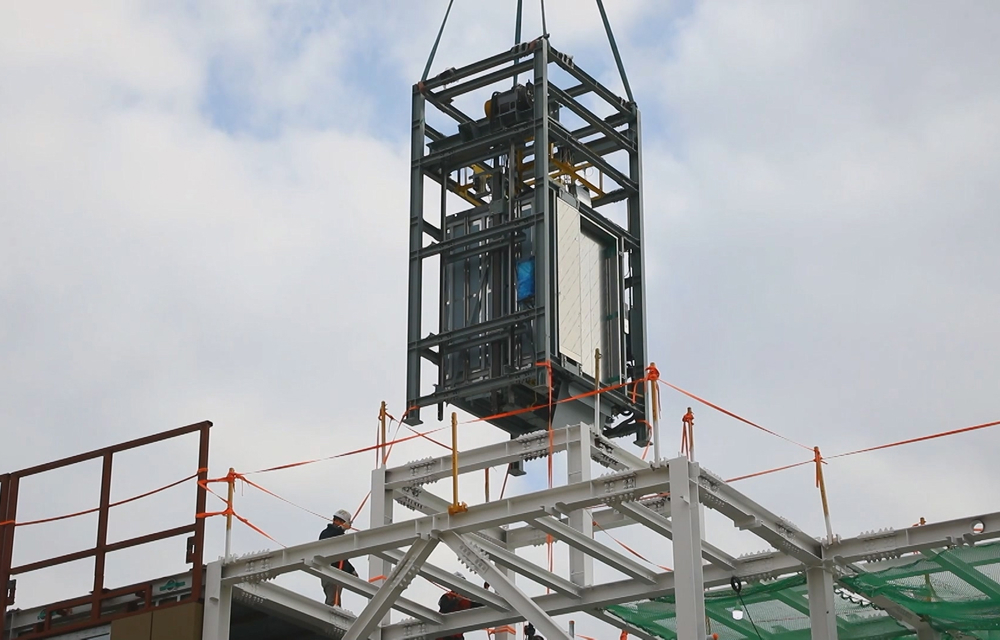 A prefabricated modular elevator system being lifted into place on a steel frame structure, illustrating integrated systems in modular construction.