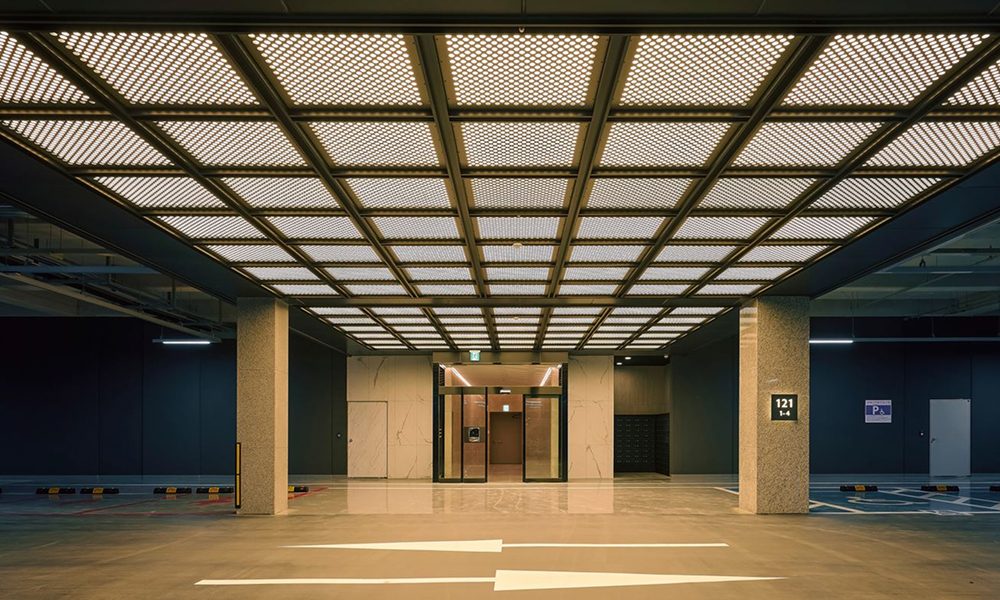 A sleek and modern residential parking space at High-End ONE PARK, designed with a hotel-inspired aesthetic. The ceiling features a geometric grid pattern with warm lighting, creating a sophisticated and welcoming atmosphere.