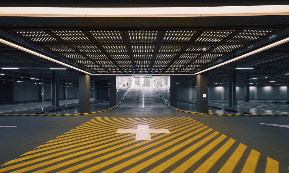 A well-lit residential parking space at High-End ONE PARK with bold yellow-striped crosswalks. The structured ceiling and reflective floor enhance visibility, ensuring safety and ease of navigation for residents.