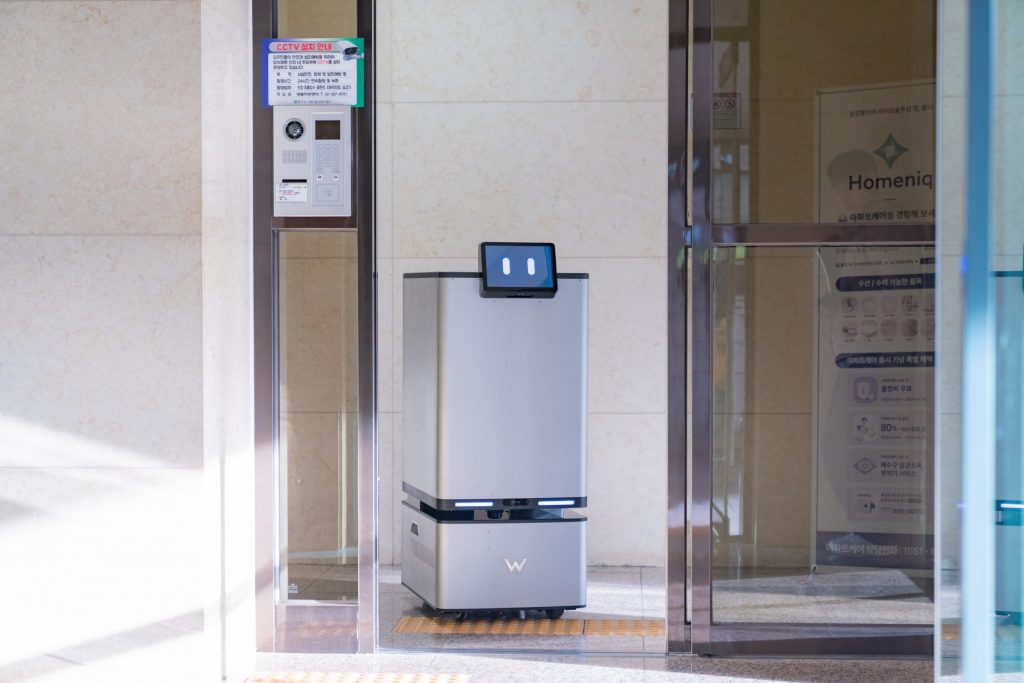 Carry Robot with a digital display screen is positioned at the entrance of an apartment complex, ready to transport heavy items.