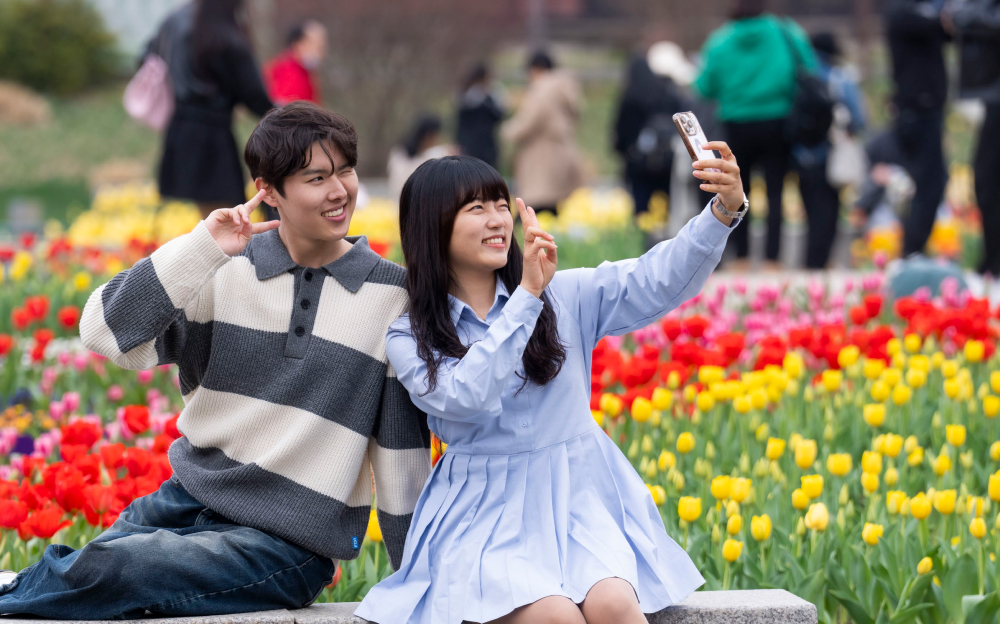 A smiling couple taking a selfie in front of a vibrant tulip garden at Everland in spring.