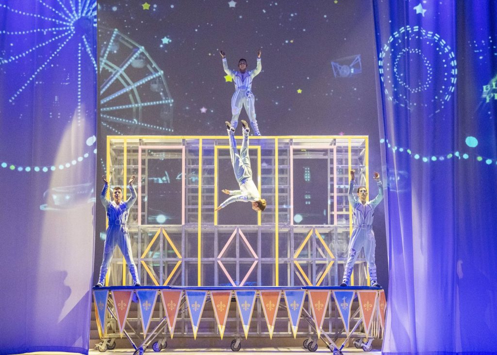Acrobats in blue jumpsuits perform a trampoline routine on stage at Everland’s Lenny’s Colorful Dream show, with one performer flipping mid-air against a whimsical night sky backdrop.