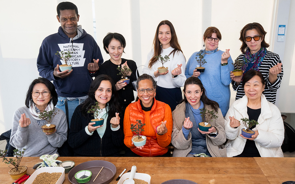 Smiles and finger hearts mark the end of a meaningful experience, as guests proudly hold their finished bonsai creations