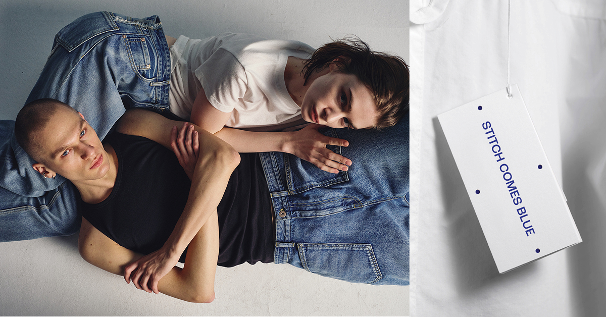 Two models lie intertwined on the floor, styled in denim from Stitch Comes Blue’s SS25 collection. The male model wears a black sleeveless top with light-wash jeans, while the female model pairs a white T-shirt with mid-wash denim. Their pose captures intimacy and contrast, highlighting the collection’s refined yet experimental edge.