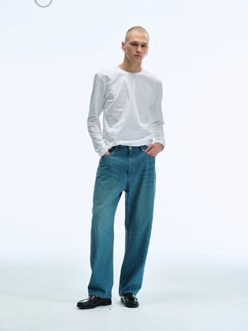 A male model stands in a studio wearing Men Straight Fit Denim Pants in Blue with a white long-sleeve T-shirt and black shoes, showcasing a relaxed yet refined silhouette.
