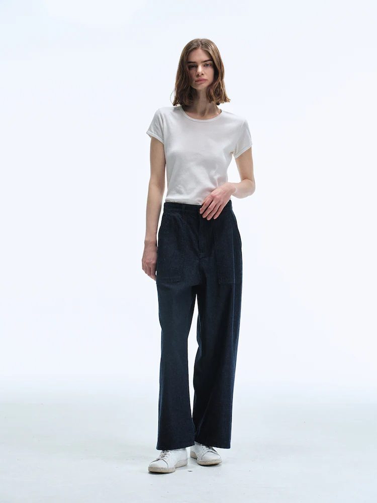 A female model poses in a studio wearing Women Selvedge Loose Straight Fit Denim in Deep Navy with a simple white T-shirt and white sneakers, highlighting the structured yet relaxed fit and rich indigo tone.