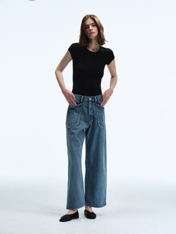 A female model stands in a studio wearing Women Straight Fit Denim Pants in Sky Blue with a short-sleeve black T-shirt and black flats, showcasing the jeans’ wide-leg silhouette and soft sky-blue wash.