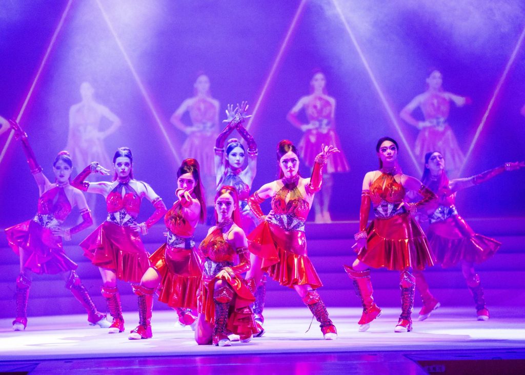 Performers in matching red costumes strike dramatic poses under colorful stage lighting during a dance sequence in Everland’s Lenny’s Colorful Dream show.
