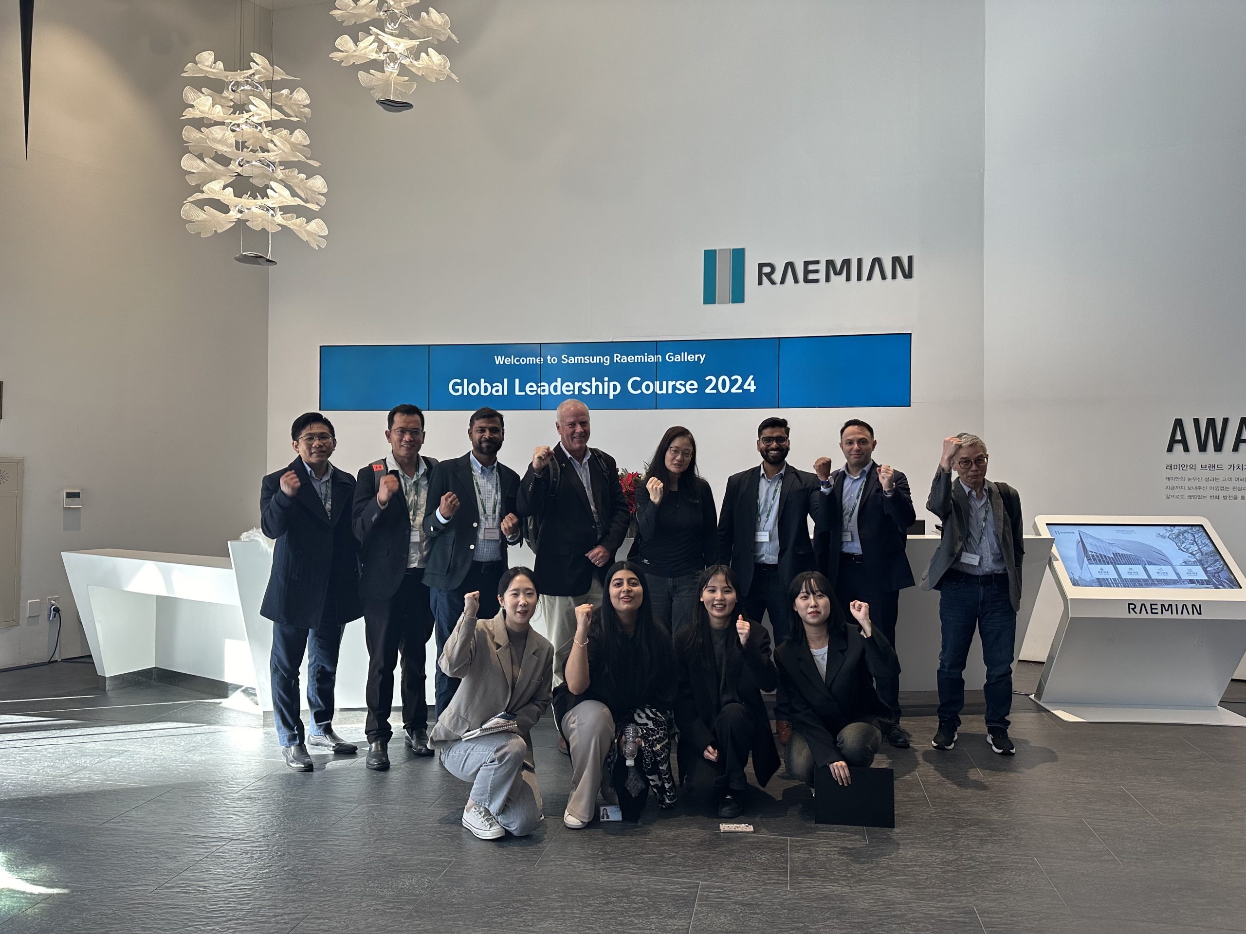 A group photo of Samsung C&T E&C employees from various departments, celebrating their participation in the 2024 Global Leadership Course, in front of the RAEMIAN gallery.