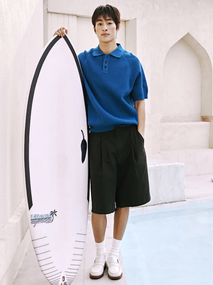 Model walking in 8seconds Bermuda Denim Shorts in Navy, styled with a striped T-shirt, loafers, and white tote. The shorts are made from 100% cotton and feature a loose fit that hits below the knee.
