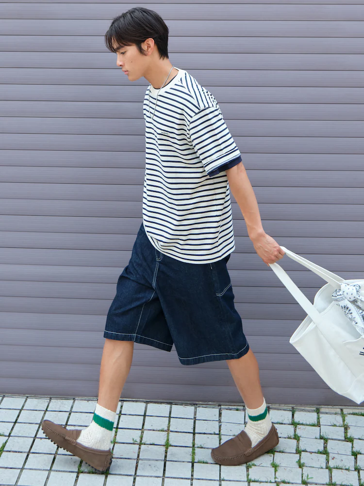 Model poses with a surfboard wearing 8seconds Black Pleated Bermuda Shorts paired with a blue knit polo. The shorts fall just over the knee and feature a relaxed, contemporary silhouette.