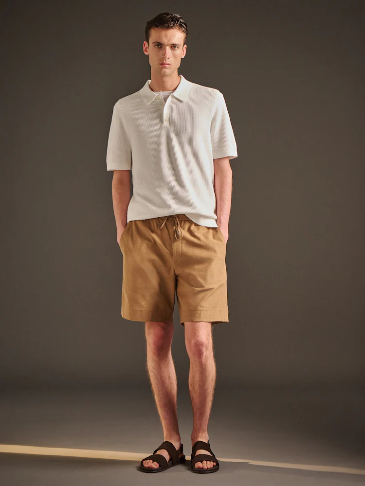 Model wears Theory Soft Terry Shorts in a camel-toned shade, styled with a cream polo knit. The look combines breathable terry fabric with minimalist design, ideal for polished warm-weather outfits.