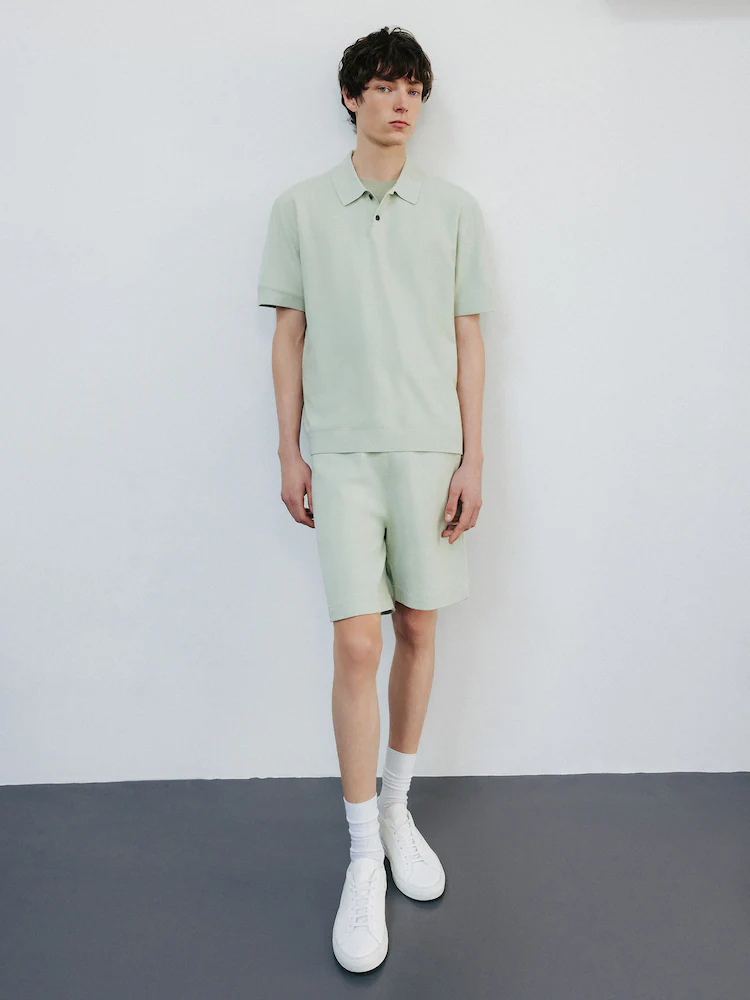 Model poses in a matching set featuring Theory Light Greenstone Sweat Shorts and a polo-style top. The pastel tone and minimal lines create a soft yet structured look.