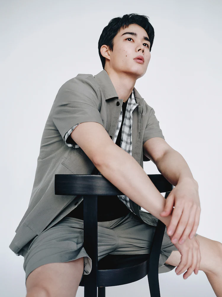 Model sits wearing ShiftG khaki cargo-style shorts paired with a coordinating short-sleeve shirt. The look mixes classic detailing with a modern relaxed cut.