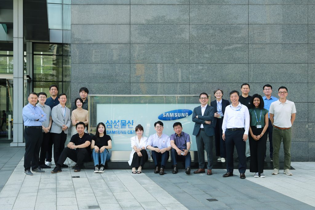 A large group photo of Samsung C&T’s Data Center Business Team standing and sitting in front of the company sign outside headquarters. 