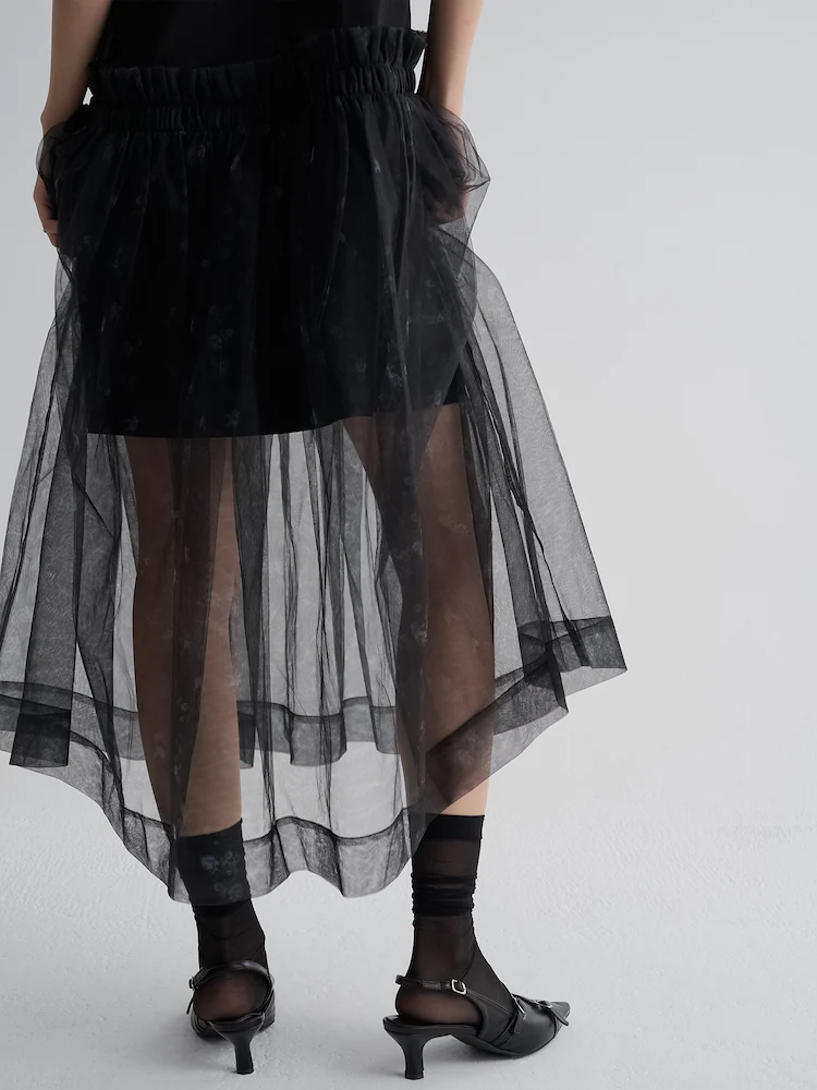 Back view of the 8seconds MINJUKIM Sheer Long Frill Dress in Black. The garment combines a fitted inner layer with a flowing sheer outer skirt, gathered at the waist for dimension. The see-through fabric enhances the romantic aesthetic with graceful transparency.