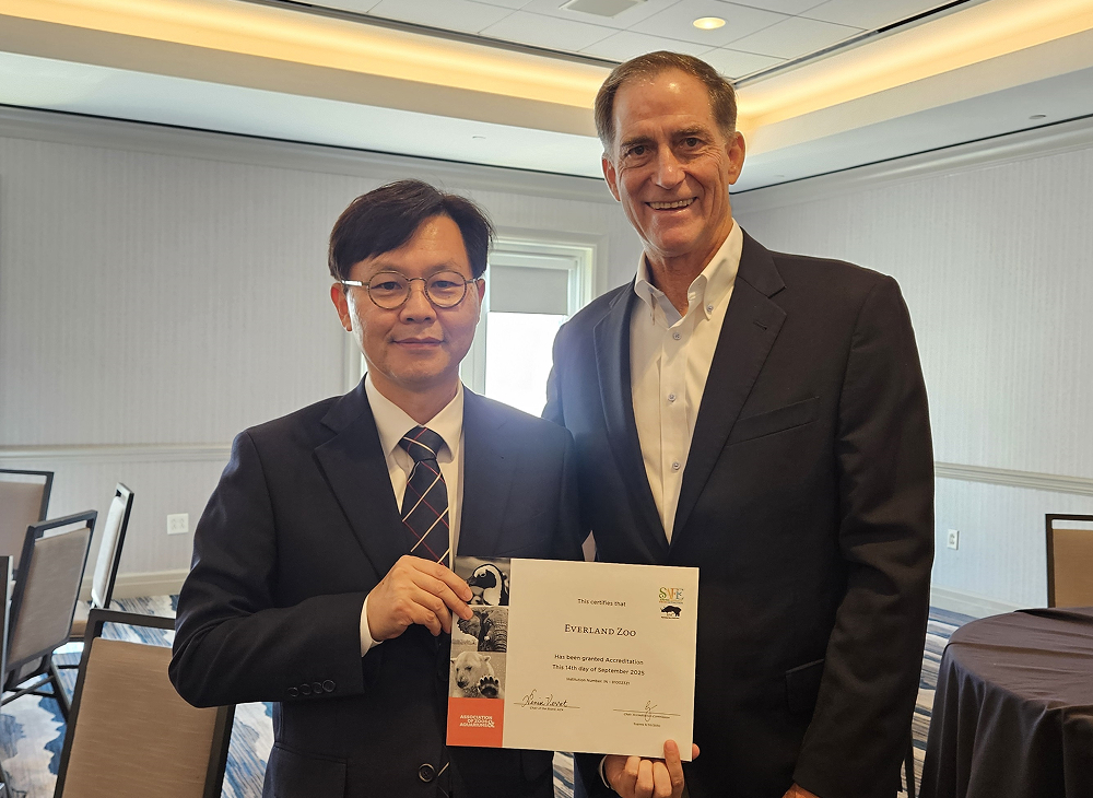 Everland Zoo representative stands with an AZA official in a conference room, holding the AZA reaccreditation certificate together and smiling for a commemorative photo.