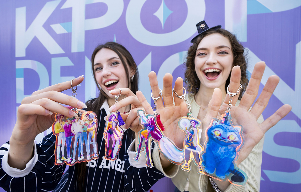 Two visitors smiling and holding up KPop Demon Hunters character keychains at Everland.